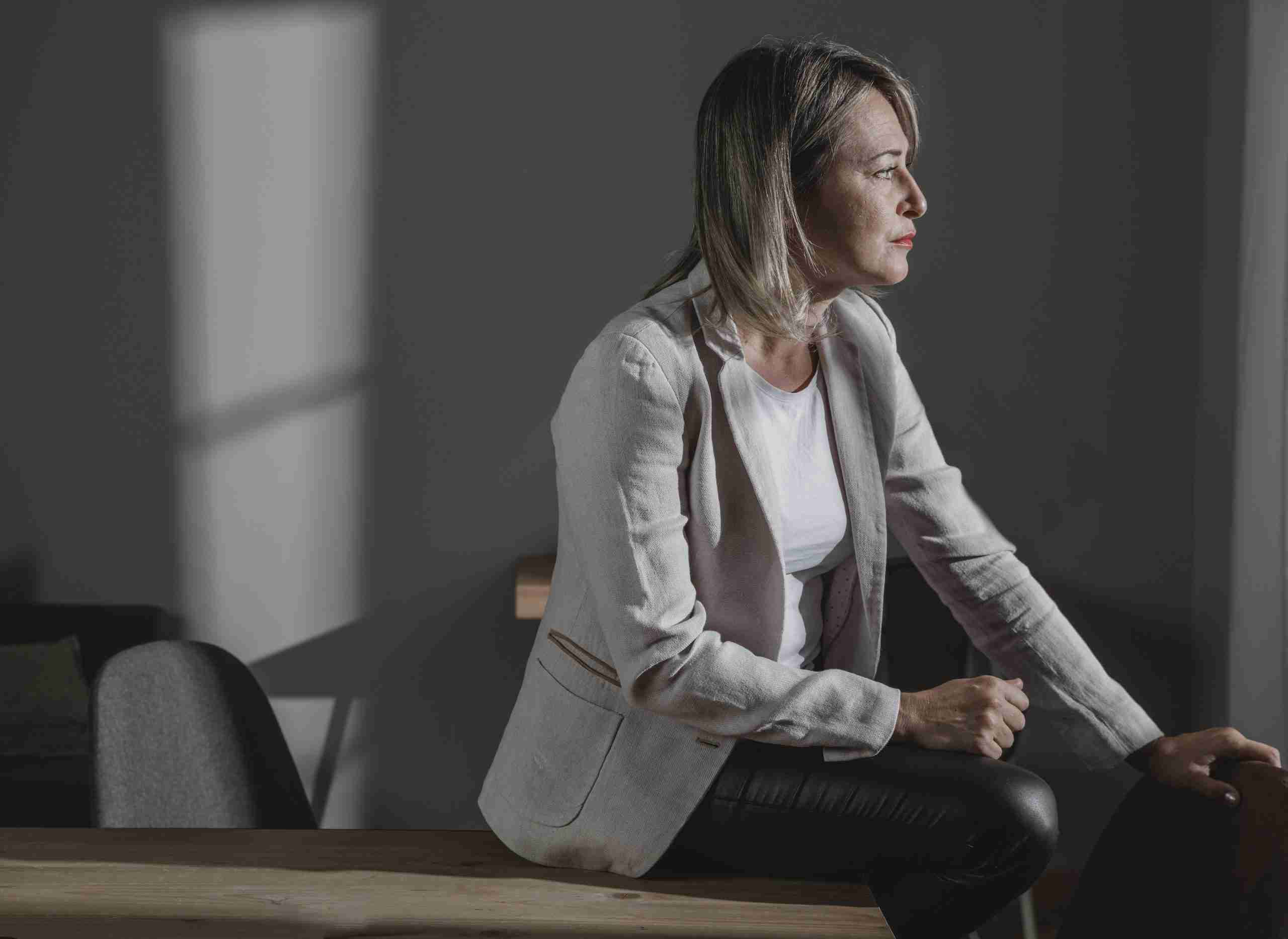 Woman suffering from chronic pain in a sweater, at home, staring out the window