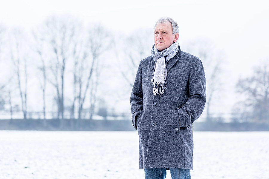Sad man wearing winter coat and scarf standing in a field of snow