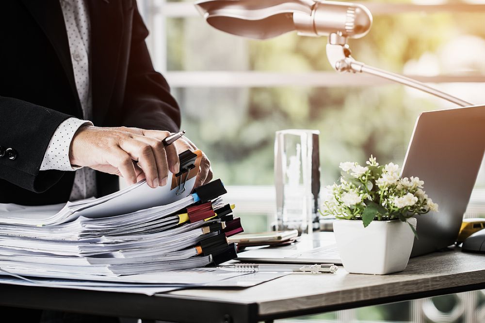 Stacks of clipped documents on a desk with a man's hands going through the docs