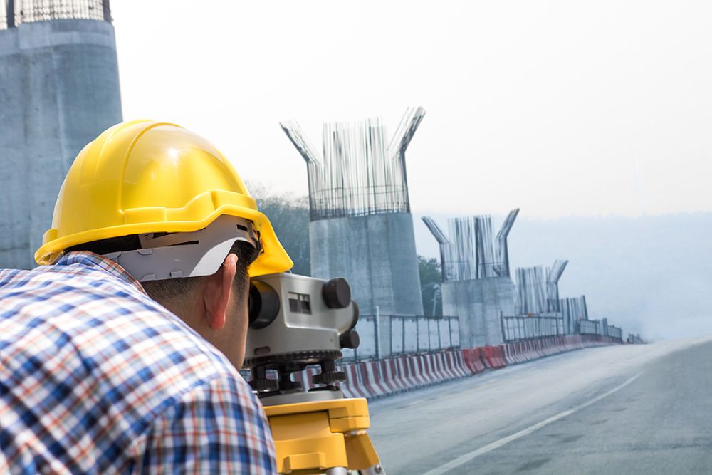 Engineer in hard hat measuring roadway under construction in the distance