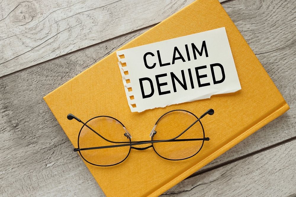Page of paper reading Claim Denied resting on top of manilla envelope